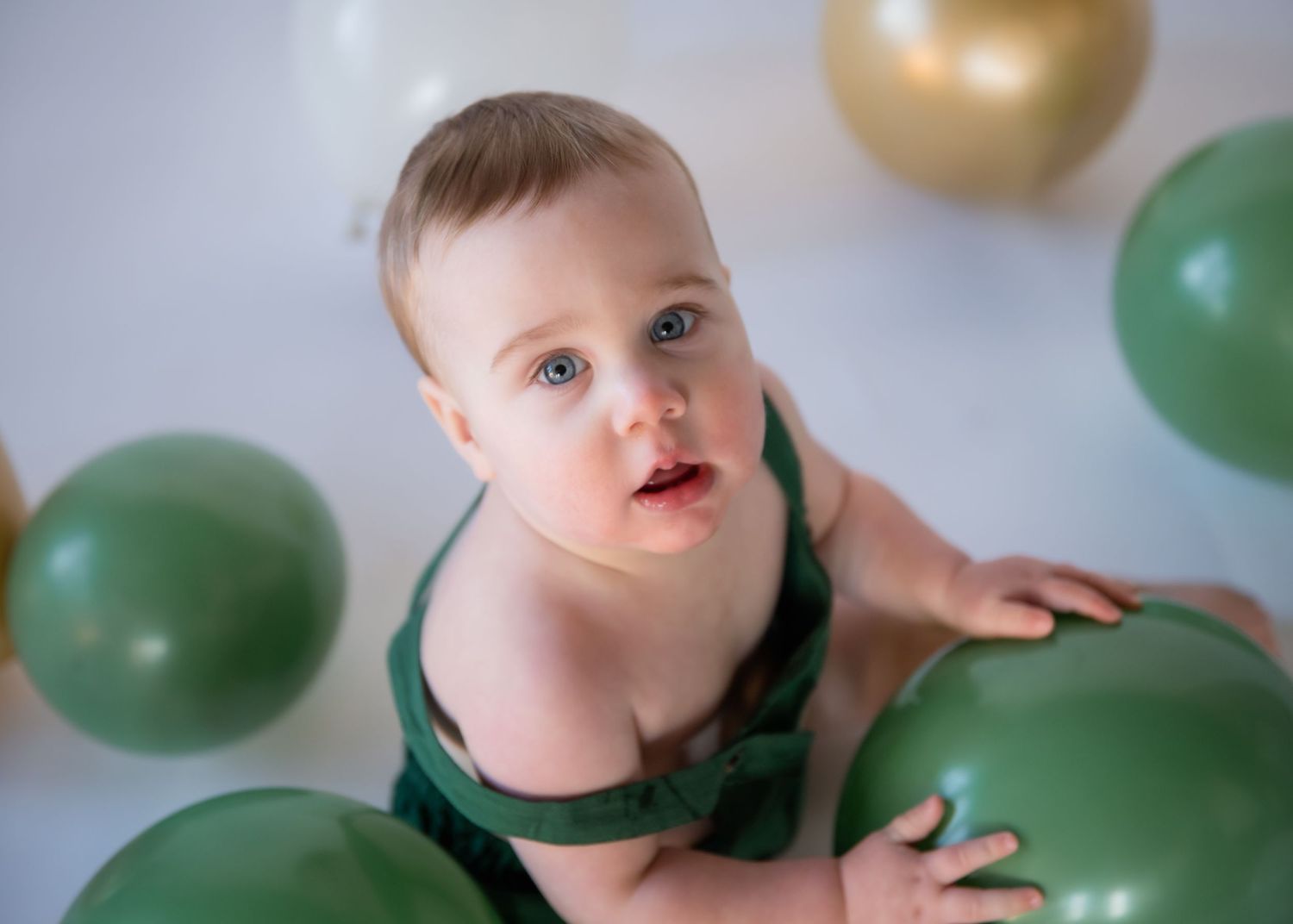 Small child in green outfit playing with gold and green balloons during a photo session.