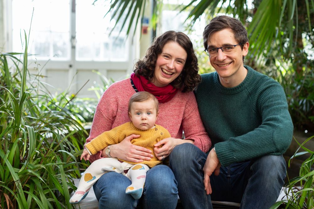 Family portrait in a greenhouse with tropical plants surrounding them.