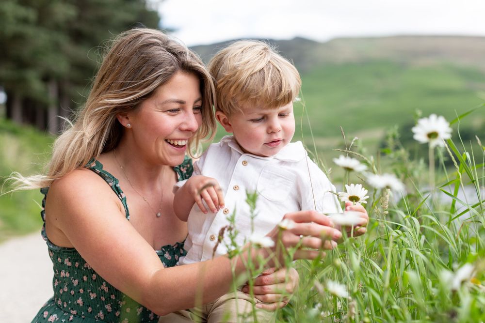 Mother and child picking wildflowers together on mountain trail during summer.