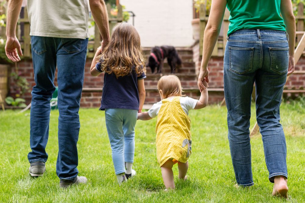 Back view of family walking together holding hands on grass lawn.