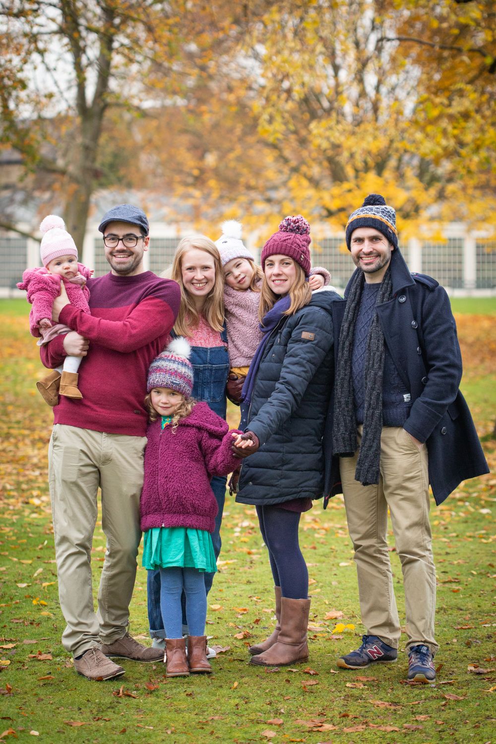 Extended family group wearing winter clothing poses together on autumn lawn.
