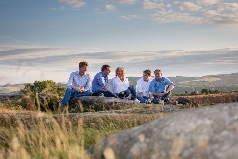 Group relaxing together on grassy hillside during golden hour with scenic countryside view.