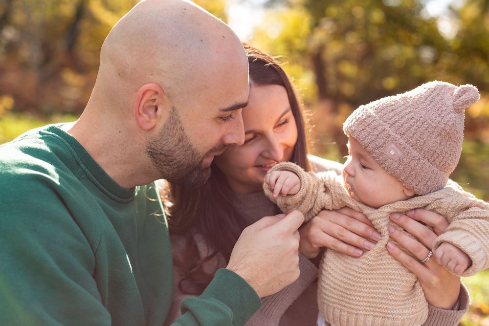 A couple sharing tender moments outdoors in autumn sunlight while wearing cozy sweaters and knit hats.