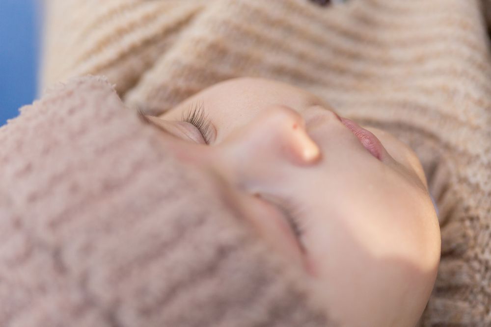 Close-up of a sleeping baby's face with soft brown blanket against blue background.