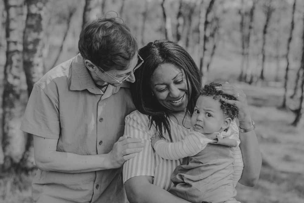 Black and white intimate family portrait in forest setting.