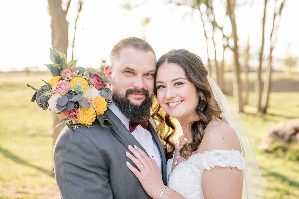 Newlyweds pose outdoors with colorful bouquet against a natural backdrop at sunset.