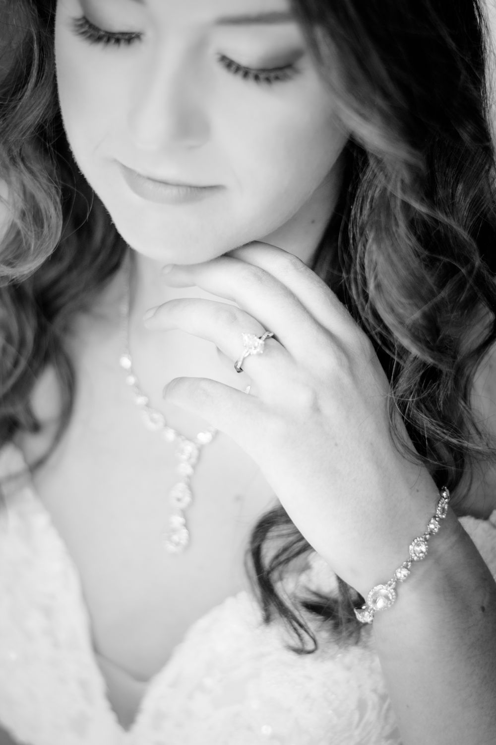 Close-up black and white portrait showing delicate jewelry and a lace wedding dress.