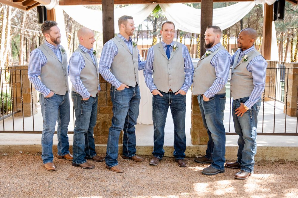 Groomsmen in matching gray vests and blue ties line up for a casual outdoor wedding photo.