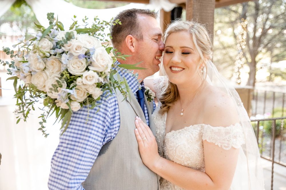 A couple shares a tender moment at their wedding celebration with a beautiful floral bouquet of white and blue flowers.