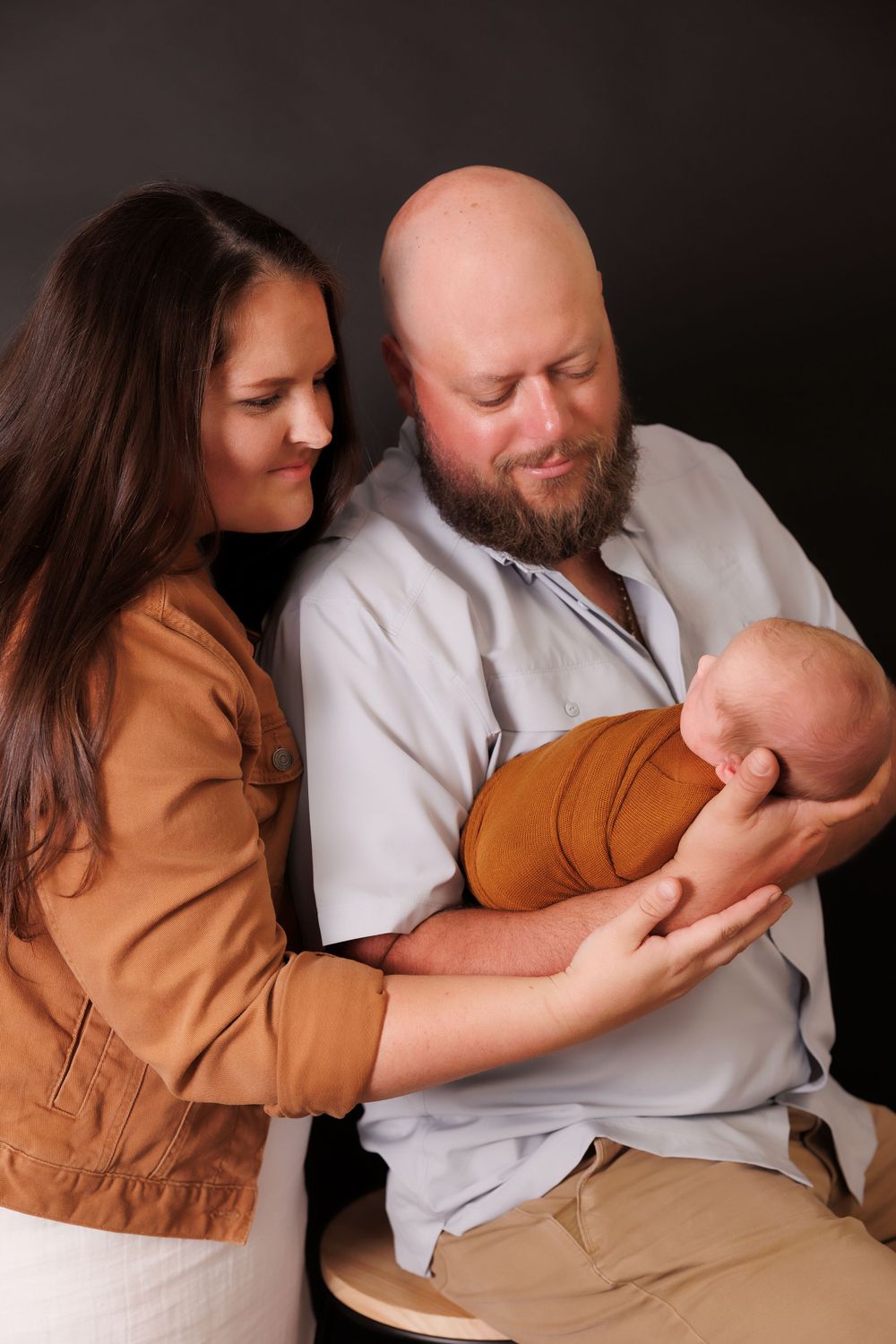 A tender family moment as parents cradle their newborn baby wrapped in brown swaddling.