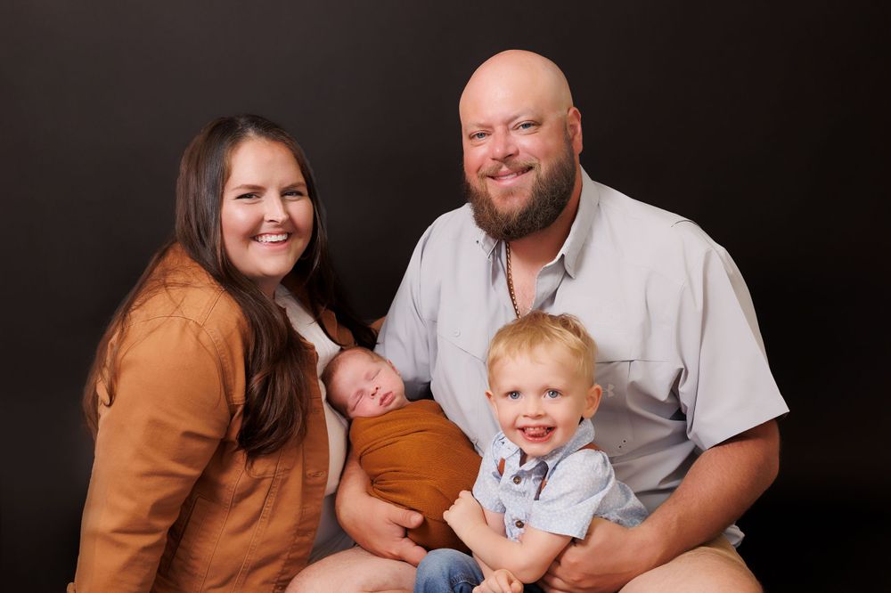 Studio portrait of a family wearing coordinated earthy tones against a dark background.