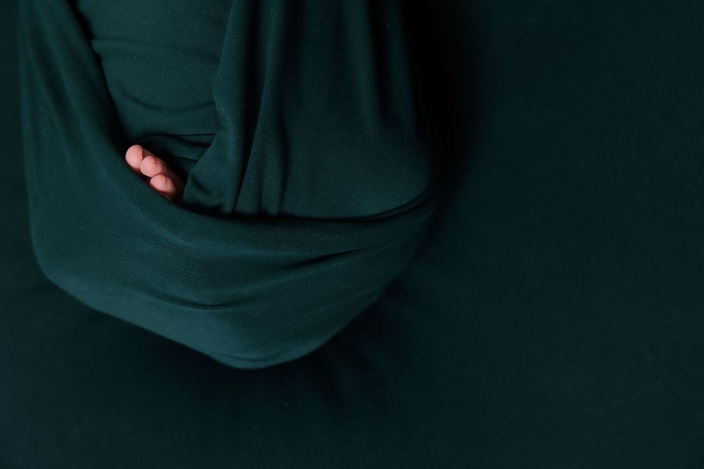 Close-up of tiny baby feet peeking out from dark teal fabric.