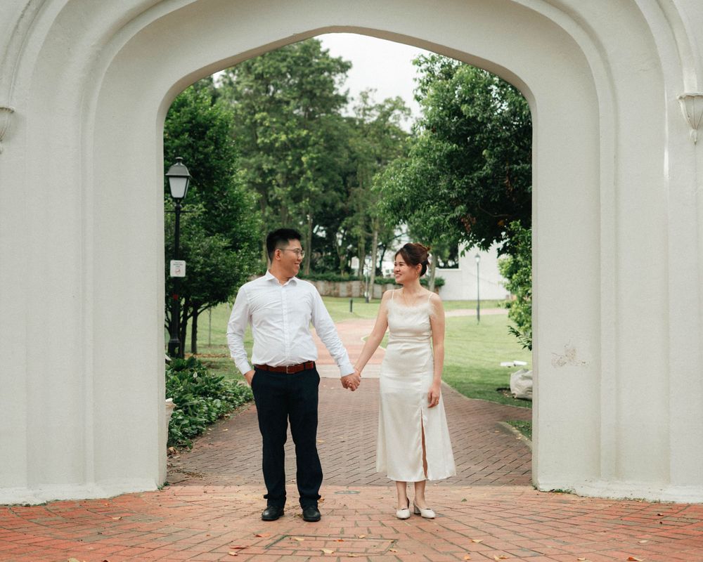 Couple in formal attire standing under a white architectural archway.