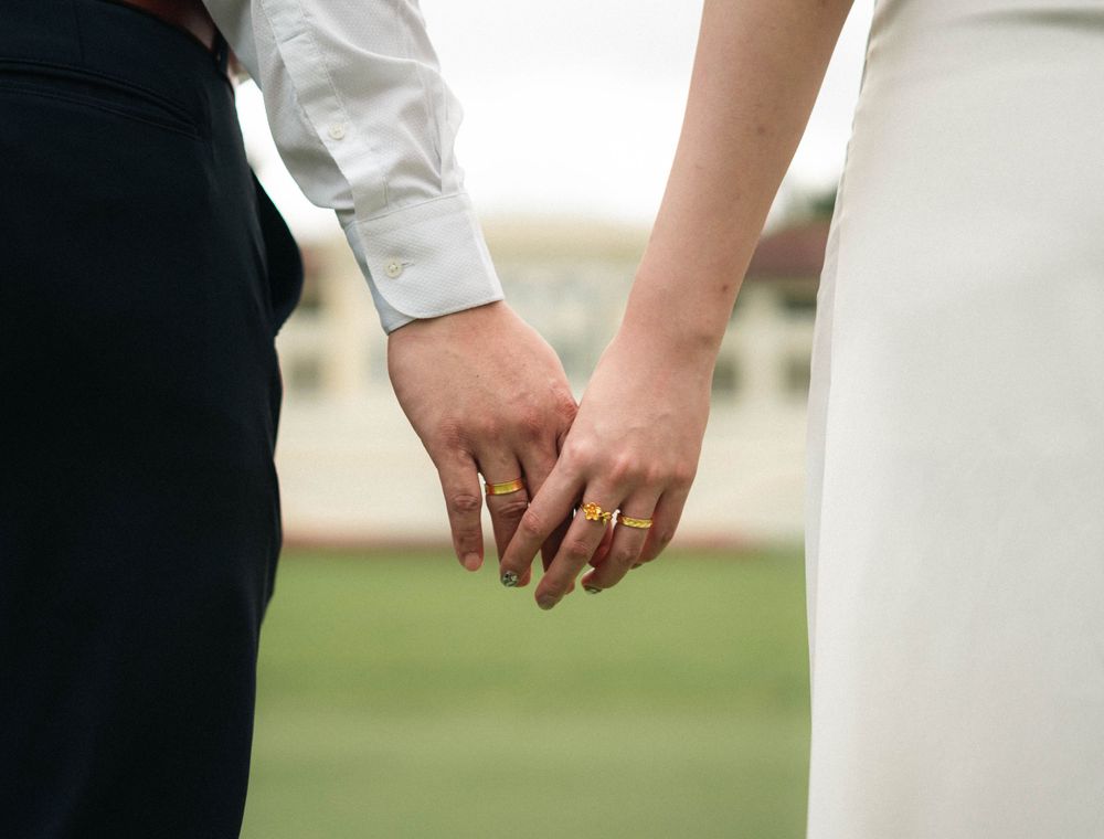 Close-up shot of a couple holding hands against a blurred outdoor background.