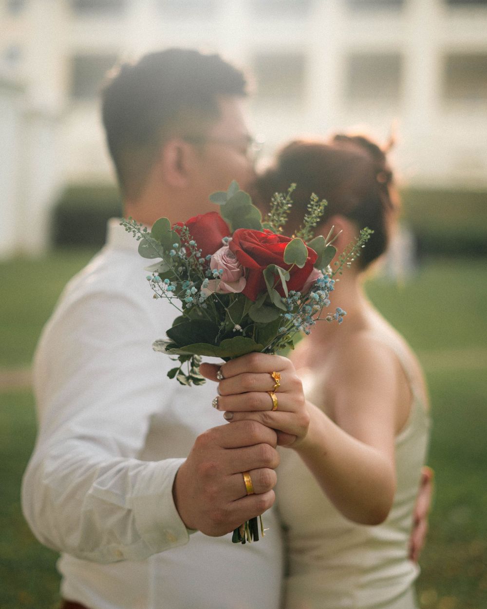 Close-up of hands holding red and pink wedding bouquet against blurred background.