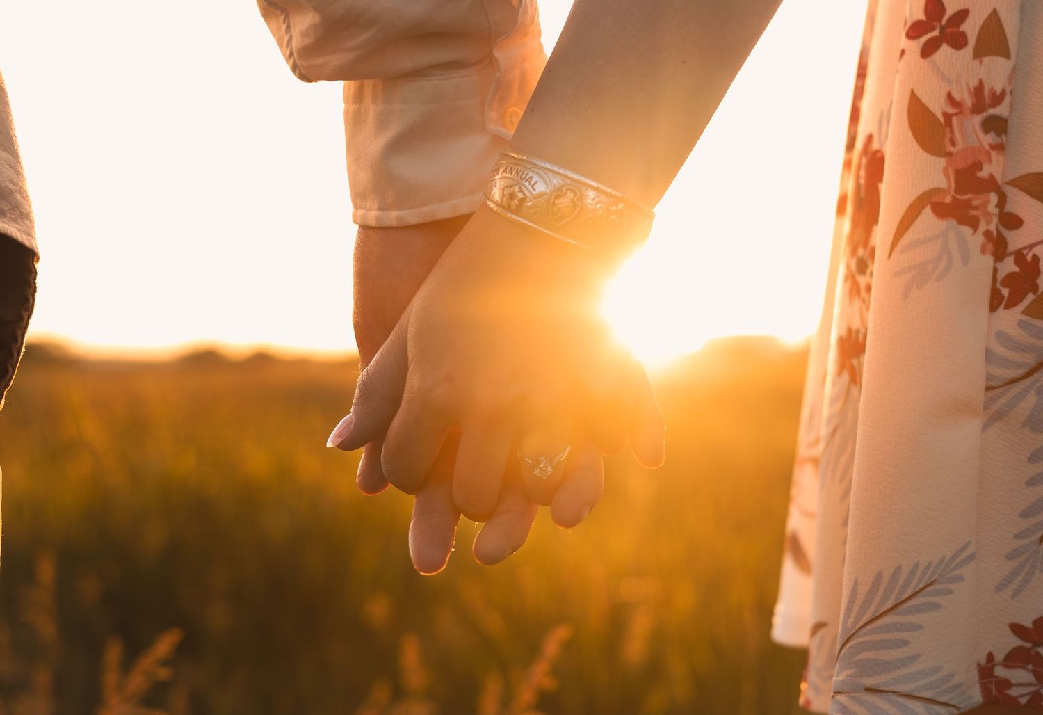 Two hands clasped together at sunset in a golden field with warm sunlight breaking through.