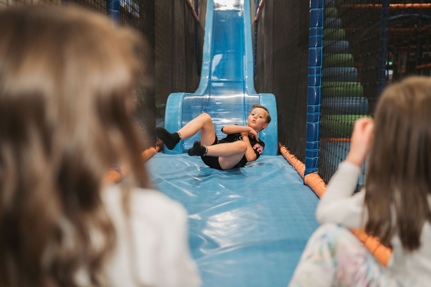 Children navigate a bright blue inflatable slide at an indoor playground.