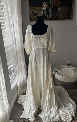 Vintage style off-white wedding dress with puff sleeves and flowing skirt displayed on black mannequin near window.