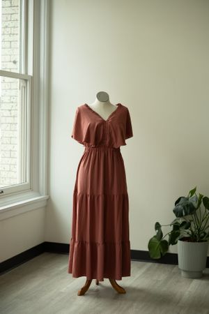 Rust colored tiered maxi dress with flutter sleeves and elastic waist shown on mannequin by window.