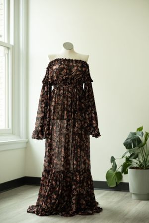 Brown floral off-shoulder maxi dress with long bell sleeves and tiered ruffle design displayed on mannequin by window.