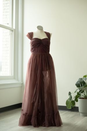 A brown tulle maxi dress with sweetheart neckline and cap sleeves displayed on a mannequin near a window.