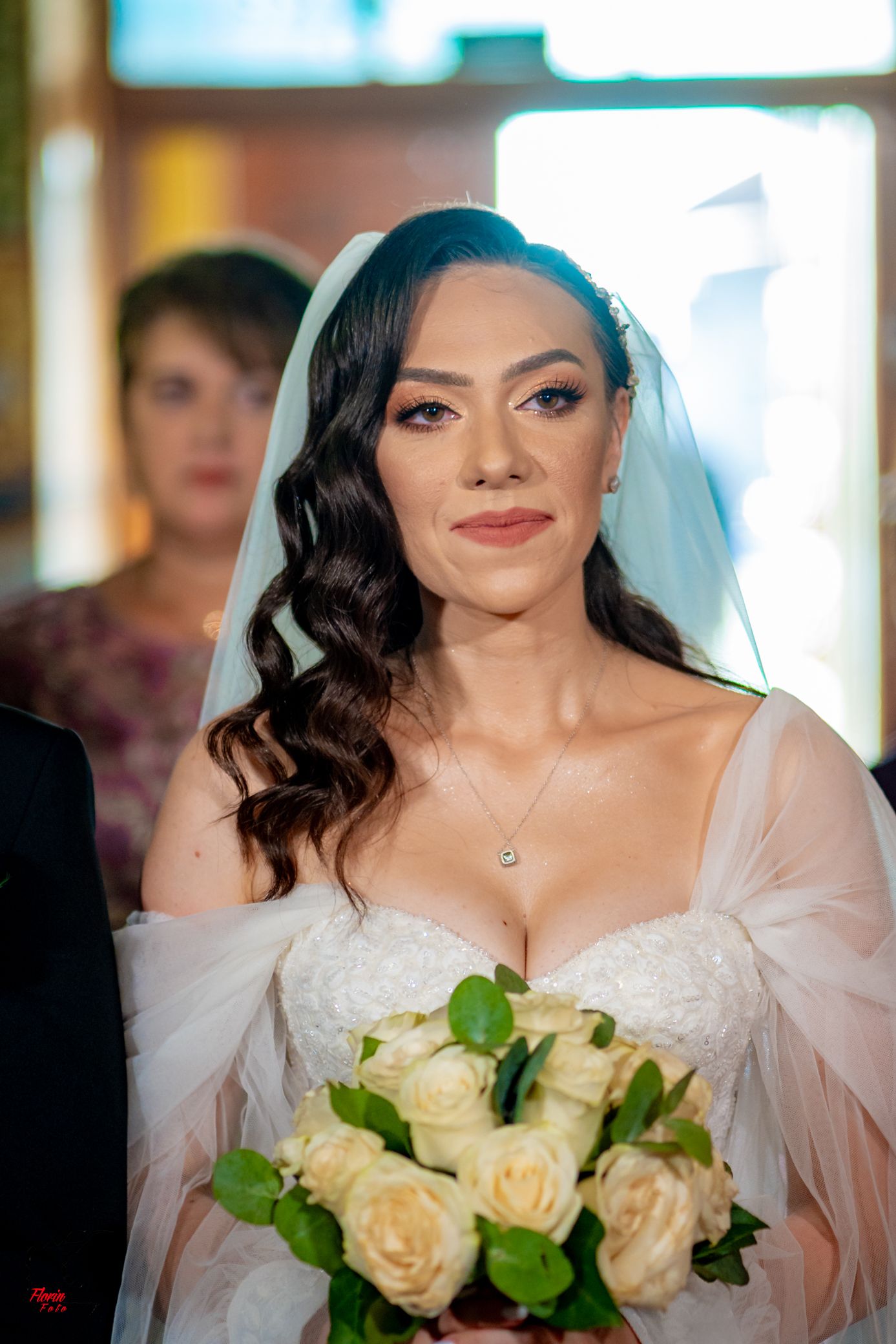Bride with long dark curls and cathedral veil smiles while holding cream rose bouquet.