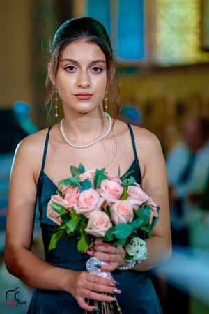 Bridesmaid in navy dress holds pink roses during wedding ceremony.