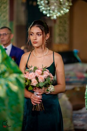 Bridesmaid in navy dress carries pink floral bouquet at evening ceremony.