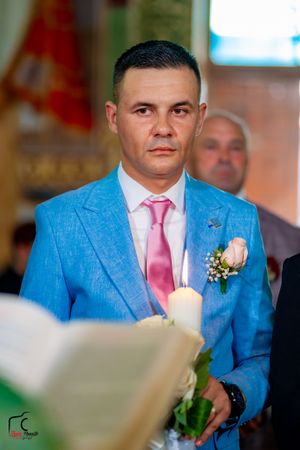 Wedding party members wearing bright blue suits with pink ties and boutonnieres stand together at a formal ceremony.