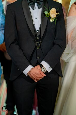 Groomsmen wearing black tuxedos and bowties stand together during wedding ceremony.