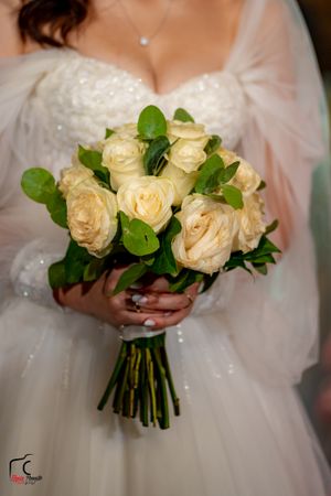 Elegant white rose and greenery bridal bouquet held against a sparkly white wedding dress.