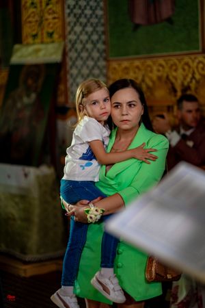 Wedding guest in bright green jacket holds small child during ceremony.