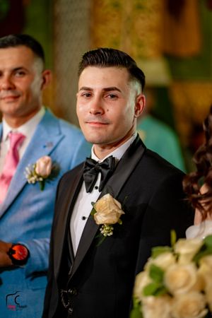 A formal wedding ceremony with guests in black tuxedos and blue suits gathered in an elegant indoor venue.