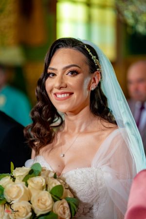 A bride in a white lace dress and veil holds a bouquet of cream roses during her wedding ceremony.