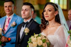 Wedding ceremony participants stand together in formal attire with cream roses and decorative lighting.