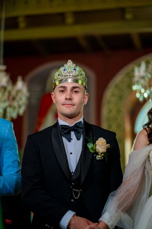 Wedding ceremony participants in formal attire standing in an ornately decorated indoor venue.