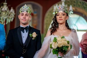 Elegant wedding ceremony with ornate crowns and white floral bouquets in a beautifully lit indoor setting.