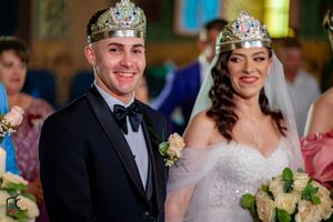 Traditional wedding ceremony with ornate crowns and white floral arrangements in warm lighting.