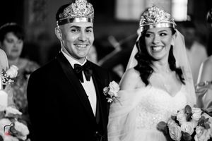 Black and white wedding photo capturing formal ceremony with crowns and bouquets.