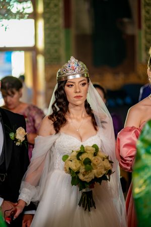 Wedding party holding cream roses and wearing ornate crowns during formal ceremony.