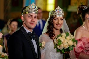 Wedding ceremony scene with decorative crowns and bouquets of cream roses in an ornate indoor setting.