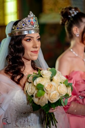 Close-up of a bridal bouquet with cream roses and a decorative crown during a wedding ceremony.