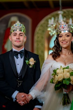 Wedding couple during ceremony wearing traditional crowns and formal attire in a church setting.
