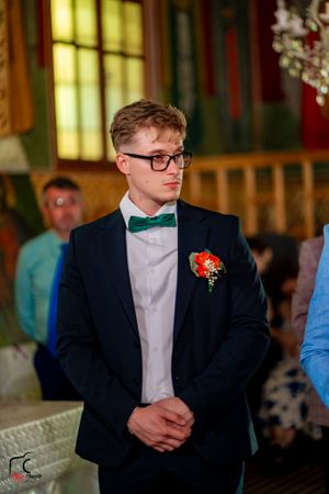 A groomsman in a black suit and green bowtie stands during a wedding ceremony.