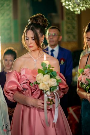 Bridesmaids wearing pink off-shoulder dresses hold floral bouquets in an ornate venue.