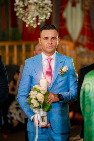 A groomsman in a light blue suit with pink tie holds a white rose bouquet.