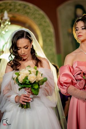 Wedding party members in pink and white dresses hold cream-colored rose bouquets.