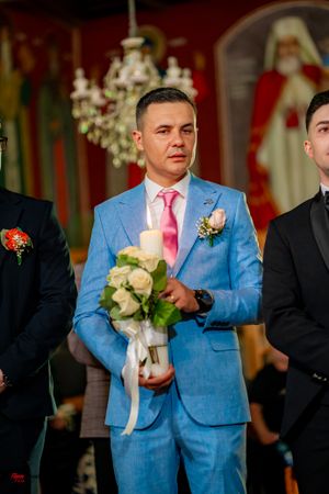 Groomsmen in formal attire stand at altar with light blue suit and pink tie in center holding white bouquet.