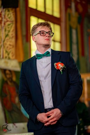 Groomsman in navy suit and bow tie with boutonniere stands in ornate church setting.