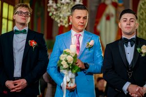 Three groomsmen in formal attire stand at altar wearing coordinated suits and boutonnieres.